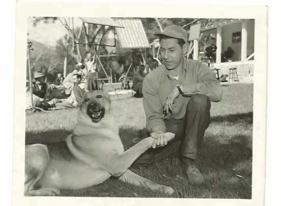 black and white photo of Paul Wurtzel and famous acting dog Flame shaking hands on location in Hollywood, circa 1947